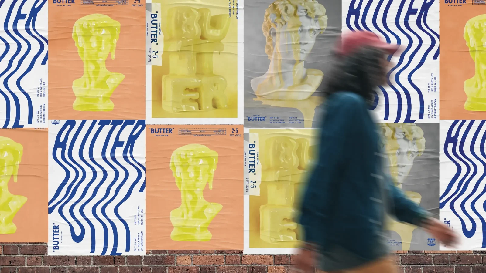 a woman walking in front of a wall covered in posters for butter art fair
