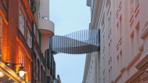A sky bridge with a spiraling metal exterior joining two buildings of different, older architectural styles