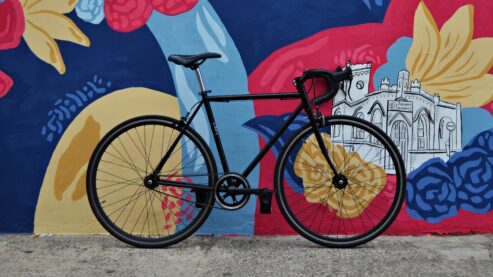 An all-black bicycle with racing-style handlebars leaning against a wall covered in a multicolor mural