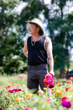 man wearing a hat and holding flowers while standing in a field of brightly colored flowers
