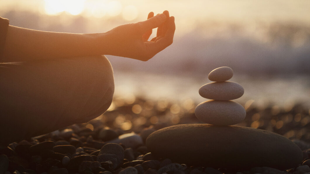 person in yoga pose next to a stack of pebbles